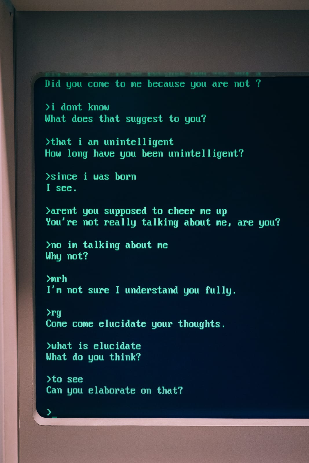 Photo of a screen at the Berlin video game museum showing an ELIZA conversation in green letters. The program keeps answering with questions such as what that suggests to you or whether you can elaborate, adding nothing of its own.